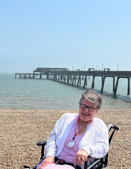 An individual in a wheelchair enjoying the beach beside the pier, embracing the seaside atmosphere